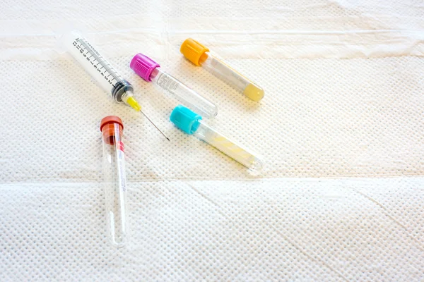 Four test tubes and a syringe on a disposable pad — Stock Photo, Image