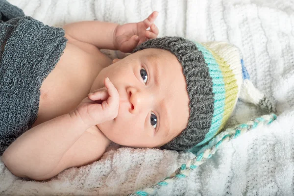 Acorda bebê com um chapéu de malha e olhos azuis com a mão na boca — Fotografia de Stock