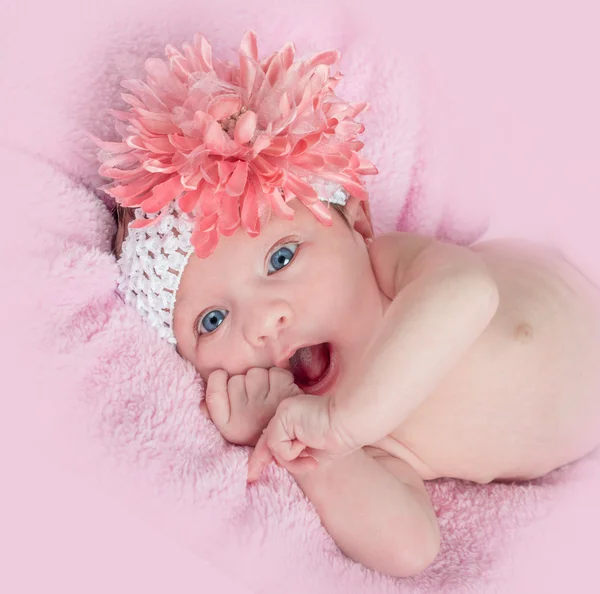 Happy blue eyed baby girl with a headband and flower