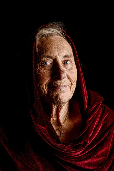 Dramatic portrait of a senior woman wearing a red shawl — Stock Photo, Image