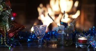 Tatil sezonu. Bir adam, şömine ateşi ve Noel süslemelerinin arka planına şişeden shot bardağına su dolduruyor. Yakın plan..
