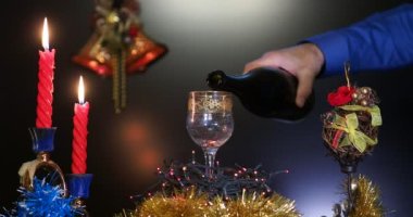Tatil sezonu. Bir adam şişeden bardağa su dolduruyor ve arka planda Noel süslemeleri, mumlar ve şenlikli bir ortam var. Yakın plan..