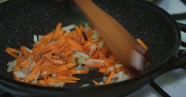 Asya mutfağı, vejetaryen. Aşçı ahşap bir spatulayla yağda kızartılmış soğan ve havuçları karıştırıyor. Yakın plan..