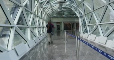 Güvenlik sistemi. Yüzünde tıbbi maske olan genç bir kadın teftiş kapısının önünde uzun bir koridorda yürür ve telefonuyla fotoğraf çeker..