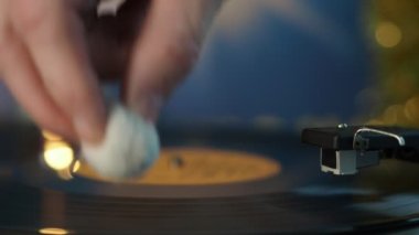 Vinil plak çalar. Bir parça dinlemeden önce plaktan bir toz kaldırır. Yakın plan..