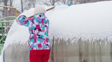 Soğutma, iklim değişikliği. Renkli kışlık elbiseli bir kadın büyük plastik bir kürekle bir çiftlikteki seradan kar temizliyor. Sibirya.