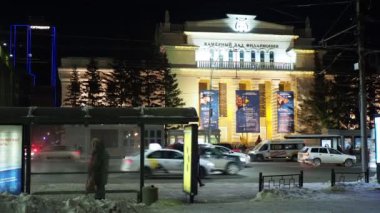 Novosibirsk, Rusya-Aralık, 12, 2021. Çok güzel aydınlatılmış Filarmoni konser salonunun arka planında toplu taşıma durağı. Elle tutulur.