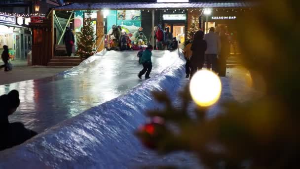 ロシアのノヴォシビルスク 2021年12月12日 ホリデーシーズンだ クリスマスだ カラーライトを背景におもちゃで装飾されたクリスマスツリーの枝やアイススライドを転がす人々 シベリア — ストック動画