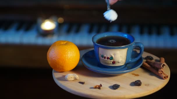 女性はピアノの鍵を背景に小さなテーブルの上に立ってお茶のカップに砂糖を注ぎ それを攪拌します パンニング クローズアップ — ストック動画