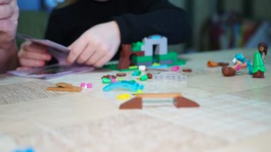 Çocuk oyunları. Yaşlı bir kadın, küçük çocukların talimatları kullanarak oyuncak evi yapmalarına yardım ediyor. Yakın plan..