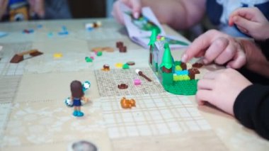 Çocuk oyunları. Yaşlı bir kadın, küçük çocukların talimatları kullanarak oyuncak evi yapmalarına yardım ediyor. Yakın plan..