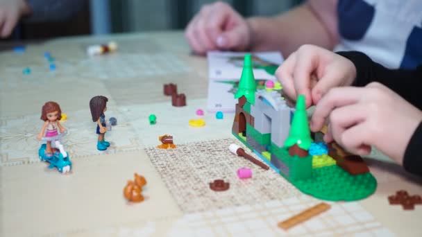 子供向けゲーム 高齢の女性は 若い子供たちが指示を使用して小さな部品からおもちゃの家を組み立てるのを助けます — ストック動画
