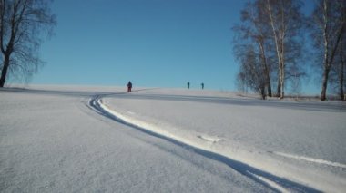 Mevsimler, kış. Kalın elbiseli üç kadın derin karlarla kaplı bir tepeden kayak yapıyor. El ele tutuş. Sibirya.