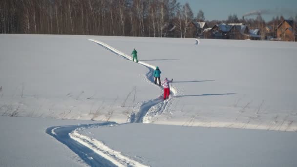 暖かい服を着た3人の女性が 住宅や石炭火力発電所の煙を背景に深い雪に覆われた丘をスキーアップしています カメラが動いてる手を握ってる シベリア — ストック動画