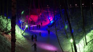 Berdsk, Rusya, Ocak, 04.2022. Tatil sezonu. Mutlu insanlar geceleri ormanda donmuş bir nehrin buzunda renkli fenerlerle süslenmiş bir vadide kayıyorlar. Sibirya.