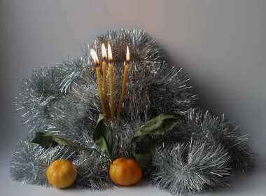 Gri arka planda dört yanan mum. Dördüncü geliyor. Ön cephede iki mandalina. Noel hazırlığı konsepti