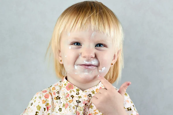 Glad liten tjej med grädde på hennes ansikte — Stockfoto