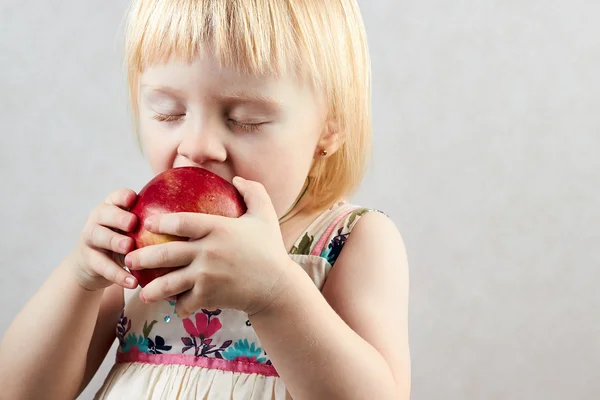 Piccola ragazza bionda morde grande mela rossa — Foto Stock