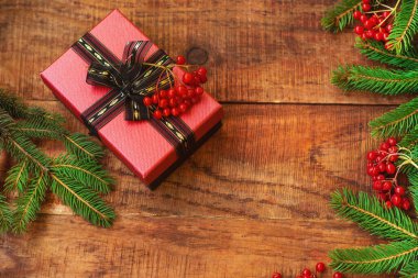 Noel arkaplanı. Spruce dalları, potasyum kırmızı böğürtlen ve ahşap arka planda bir hediye. Üst Manzara. Noel ya da yeni yıl kartı. Metin için yer, kopyalama alanı, düz uzanma