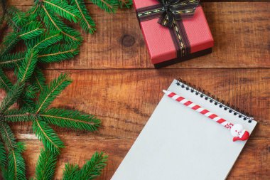 Noel arkaplanı. Yuvarlak bir çerçeve şeklinde ladin dalları, ahşap bir arka planda kalem, hediye ve defter.
