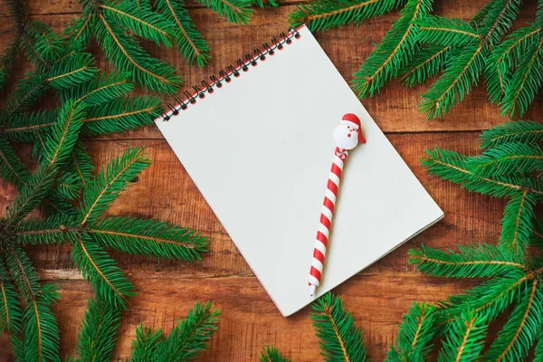Christmas background. Spruce branches in the form of a round frame and notebook with pen on a wooden background — Stock Photo, Image