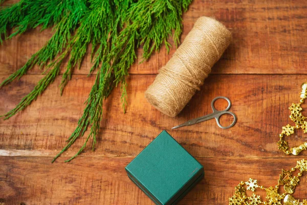 Fundo de Natal. O processo de embalar um presente de Natal. Tesoura, enrolamento de rosca, caixa em um fundo de madeira — Fotografia de Stock