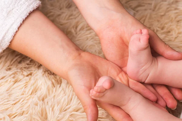 Η μαμά κρατάει στα χέρια της ένα μικρό ποδαράκι. Μικρά πόδια νεογέννητου μωρού στα χέρια της μητέρας. Μασάζ ποδιών μωρού — Φωτογραφία Αρχείου