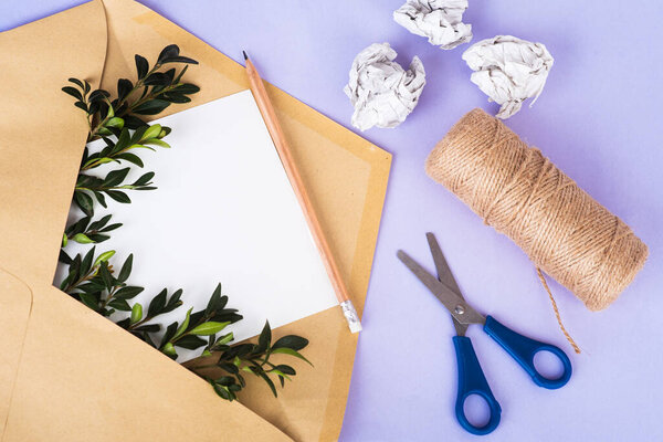 Открытый бумажный конверт с пустой бумагой и зелеными веточками среди скомканной бумаги и обмотки связки изолированы на фоне Very Peri. Концепция нулевых отходов. Органический материал. Вид сверху, пространство для копирования