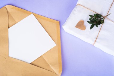 Opened craft paper envelope with empty white paper, gift in eco package with green twigs from above on very pari background. Zero waste concept. Organic material. Top view, copy space
