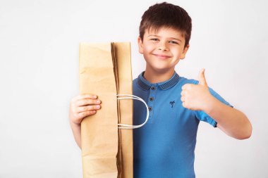 Kese kağıdıyla gülümseyen sevimli çocuk, onay vermeme işareti gösteriyor, çevre dostu şeylerin kullanımını teşvik ediyor. Beyaz arka planda. Boşluğu kopyala, sıfır atık kavramı