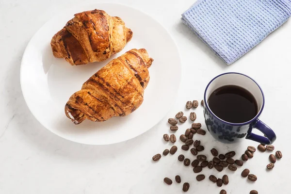 delicious, appetizing, crispy croissants, hot coffee in the blue cup and kitchen towel on plate on marble table. French pastries. Top view. Perfect breakfast. Breakfast aristocrat