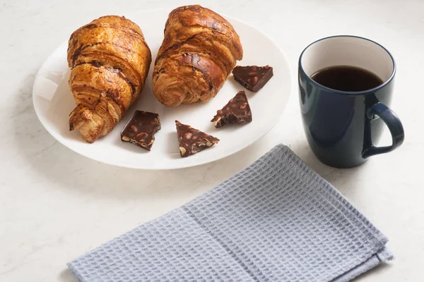 delicious, appetizing, crispy croissants with dark chocolate, hot coffee and kitchen towel on plate on marble table. French pastries. Top view. Perfect breakfast. Breakfast aristocrat