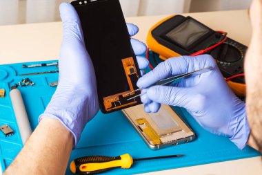 Mavi Eldiven Ustası özel bir minderdeki aletleri kullanarak bir cep telefonunu tanılar ve onarır. Düz yatış, üst manzara. cep telefonu onarımı