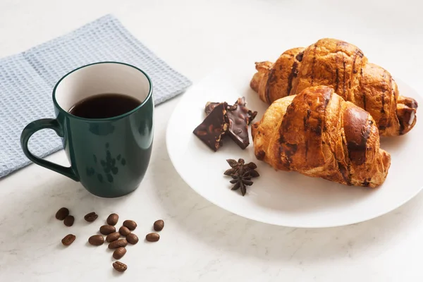 delicious, appetizing, crispy croissants, chocolate, hot coffee in the blue cup and kitchen towel on plate on the light marble table. French pastries. Top view. Breakfast aristocrat. Tasty eat