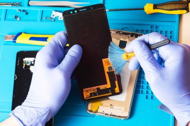 Lastik eldivenli bir zanaatkar tamir için özel bir lastik paspasın üzerindeki cep telefonunu tamir eder ya da ona hizmet eder. İçeriden bak. Cihazı tamir ediyorum. Bozuk akıllı telefon.