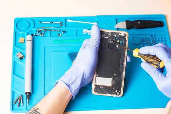 Craftsman in rubber gloves repair or service a mobile phone on a special rubber mat for repair. view from the inside. Fixing the gadget. Broken smartphone