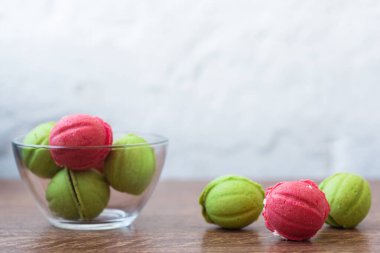 Açık arkaplandaki ahşap bir masada içi krema dolu cam şeffaf vazo içeren fındık şeklinde çok renkli kurabiyeler. Ev yapımı kurabiyeler. Uzayı kopyala Lezzetli tatlılar.