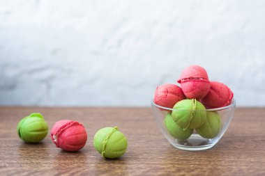 Açık arkaplandaki ahşap bir masada cam şeffaf vazoda içi krema dolu fındık şeklinde çok renkli kurabiyeler. Ev yapımı kurabiyeler. Uzayı kopyala Lezzetli tatlılar.