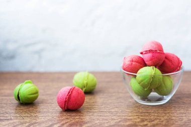 Açık arkaplandaki ahşap bir masada cam şeffaf vazoda içi krema dolu fındık şeklinde çok renkli kurabiyeler. Ev yapımı kurabiyeler. Uzayı kopyala Lezzetli tatlılar.