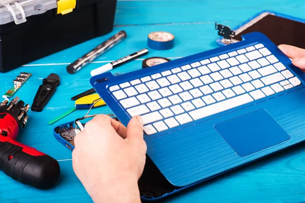 Büyücü mavi ahşap masadaki dizüstü bilgisayarı restore eder. Üst Manzara. Dizüstü bilgisayarın yedek parçalarına ayrılması. Aletleri kullanarak bilgisayar ekipmanlarının bakımı. İçerideki dizüstü bilgisayara bak