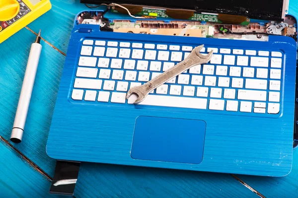 Wizard repairs laptop with tools and hands on the blue wooding table. top view. wrench and screwdriver on the keyboard