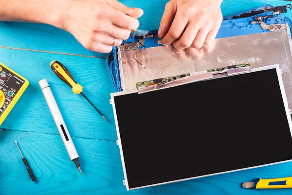 Wizard repairs laptop with tools and hands on the blue wooding table. top view