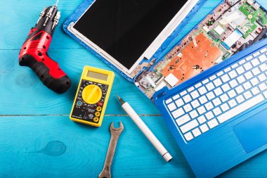 Büyücü mavi ahşap masadaki dizüstü bilgisayarı restore eder. Üst Manzara. Dizüstü bilgisayarın yedek parçalarına ayrılması. Aletleri kullanarak bilgisayar ekipmanlarının bakımı. İçerideki dizüstü bilgisayara bak