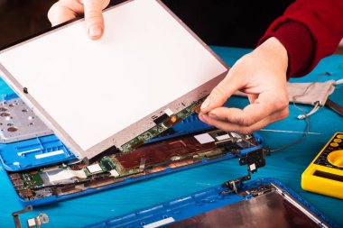 The wizard restores the laptop on the blue wooding table. top view. Disassembly of the laptop into spare parts. Maintenance of computer equipment using tools. View of the laptop inside