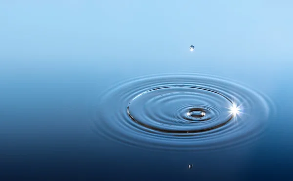 Капля изолирована в голубой воде с солнечным лучом — стоковое фото