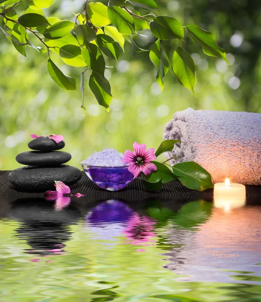 Dvě svíčky a ručníky černé kameny a purpurové kvítky na vodě — Stock fotografie