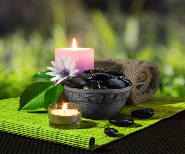 Pot van zwarte stenen en kaarsen op groene mat — Stockfoto