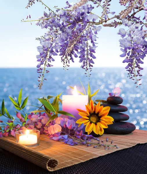 Massage stones with candles, daisy and wisteria - sea background - backlight — Stock Photo, Image