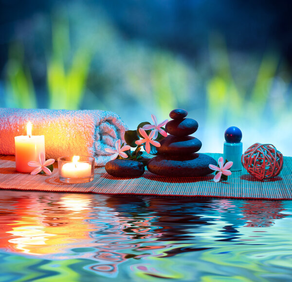 Two candles and towels black stones and tiare on water
