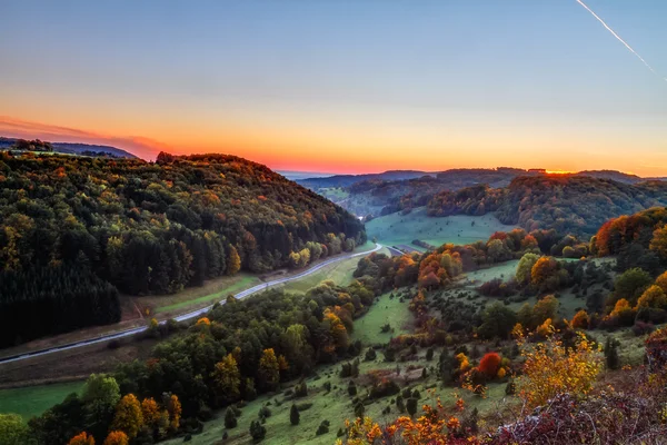 Idyllische Herbstkulisse mit farbenfrohen orange-goldenen Bäumen an einer schönen Landstraße in den felsigen Jurabergen Bayerns. Sonnenuntergang im Herbst mit herrlich klarem Himmel in der ländlichen Landschaft. — Stockfoto